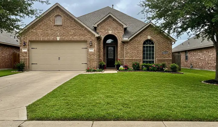 Brick home with a lush green front lawn and potted flowers at the entry