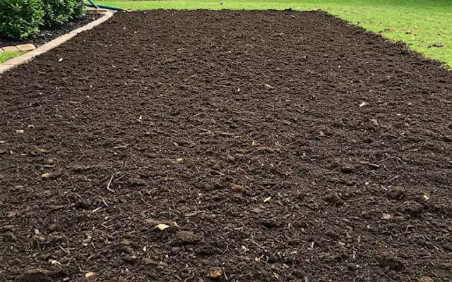 Backyard area of freshly tilled dark soil beside a lawn and wood fence