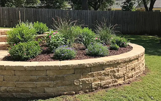 Curved block raised flower bed with perennials and ornamental grasses in a backyard