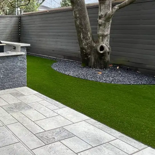 Artificial turf beside large gray pavers and a black rock tree ring in a Houston backyard