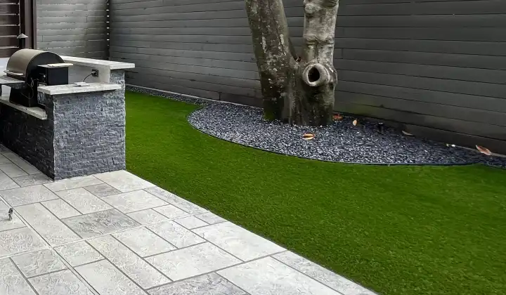 Artificial turf beside large gray pavers and a black rock tree ring in a Houston backyard
