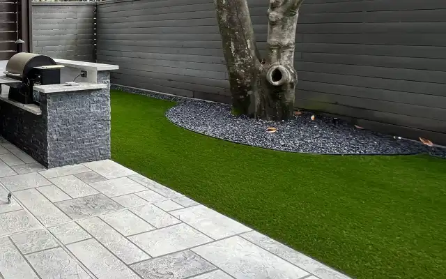 Artificial turf lawn meeting gray pavers and an outdoor grill island in a Houston backyard