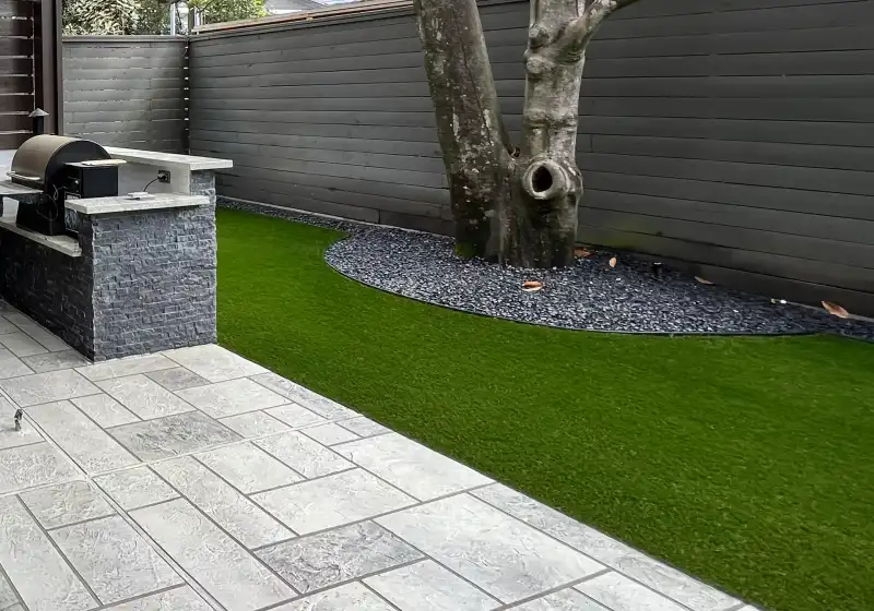 Artificial turf beside large gray pavers and a black rock tree ring in a Houston backyard