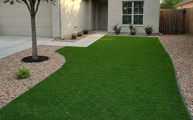 Artificial turf front lawn bordered by rock beds and a young shade tree
