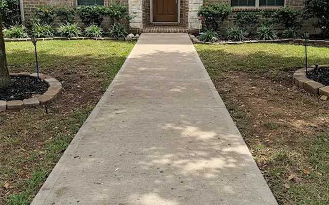 Straight broom-finish concrete walkway leading to a brick home front door