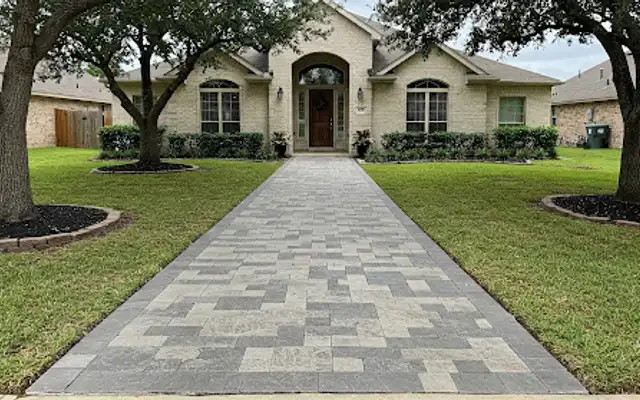 Wide gray and tan paver walkway leading across a front lawn to a home